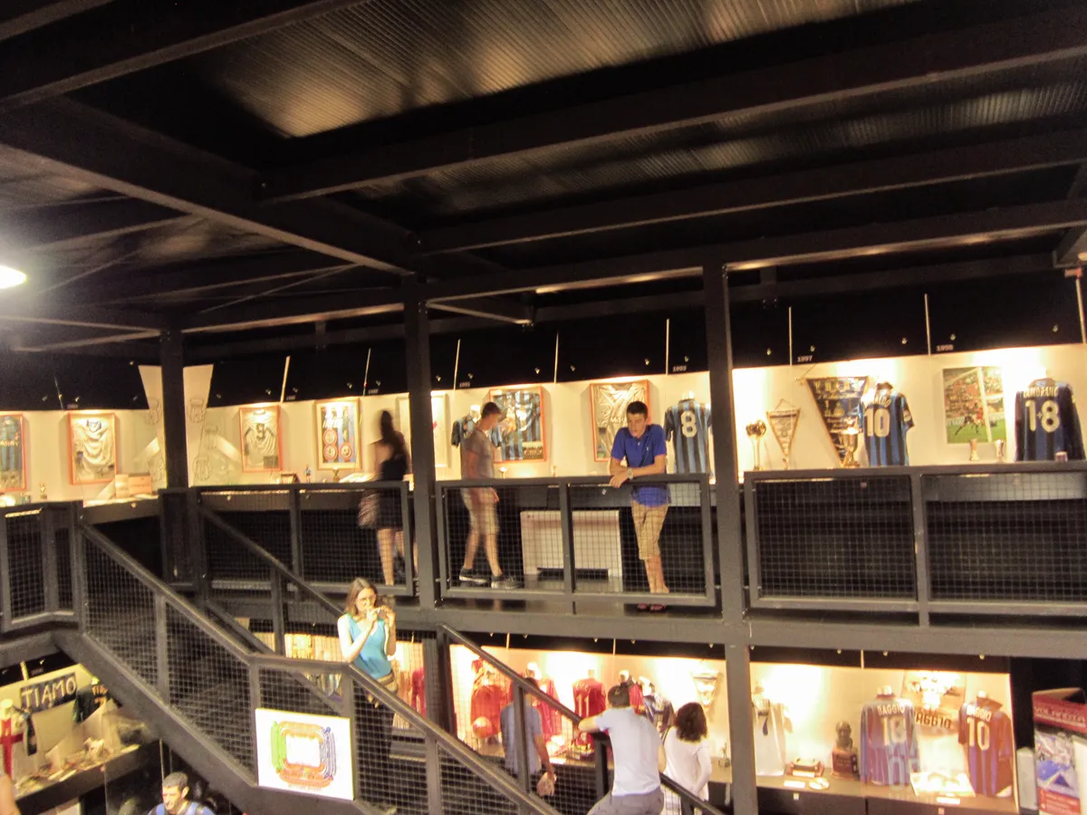 Visitors on the upper level of the San Siro museum with display cases of club memorabilia in Milan